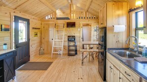 Interior de una cabaña de madera con área de cocina, que incluye un lavamanos, estufa y armarios de madera.