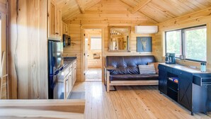 Interior de una cabaña con paredes de madera, una kitchenette, un sofá y un ventanal grande.