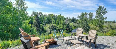 An outdoor seating area with Adirondack chairs and a wooden table, surrounded by gravel and greenery.