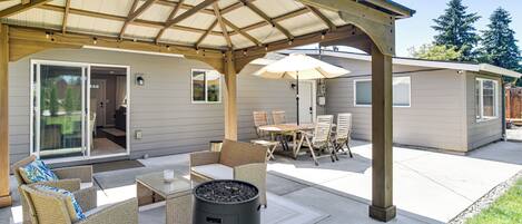 An outdoor patio with wicker furniture, a black trash can, and a covered area with a pergola.