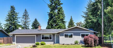 A single-story house with a garage, a small front yard, and a red bush.