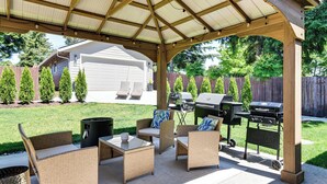 Een overdekt terras met rieten meubilair, een grill en een barbecue.
