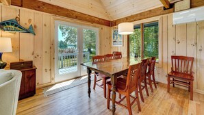 A wooden interior with a dining table and chairs, a lamp, and a view through the glass door. - Dock + Kayaks: Annabessacook Lake Retreat! (Winthrop)