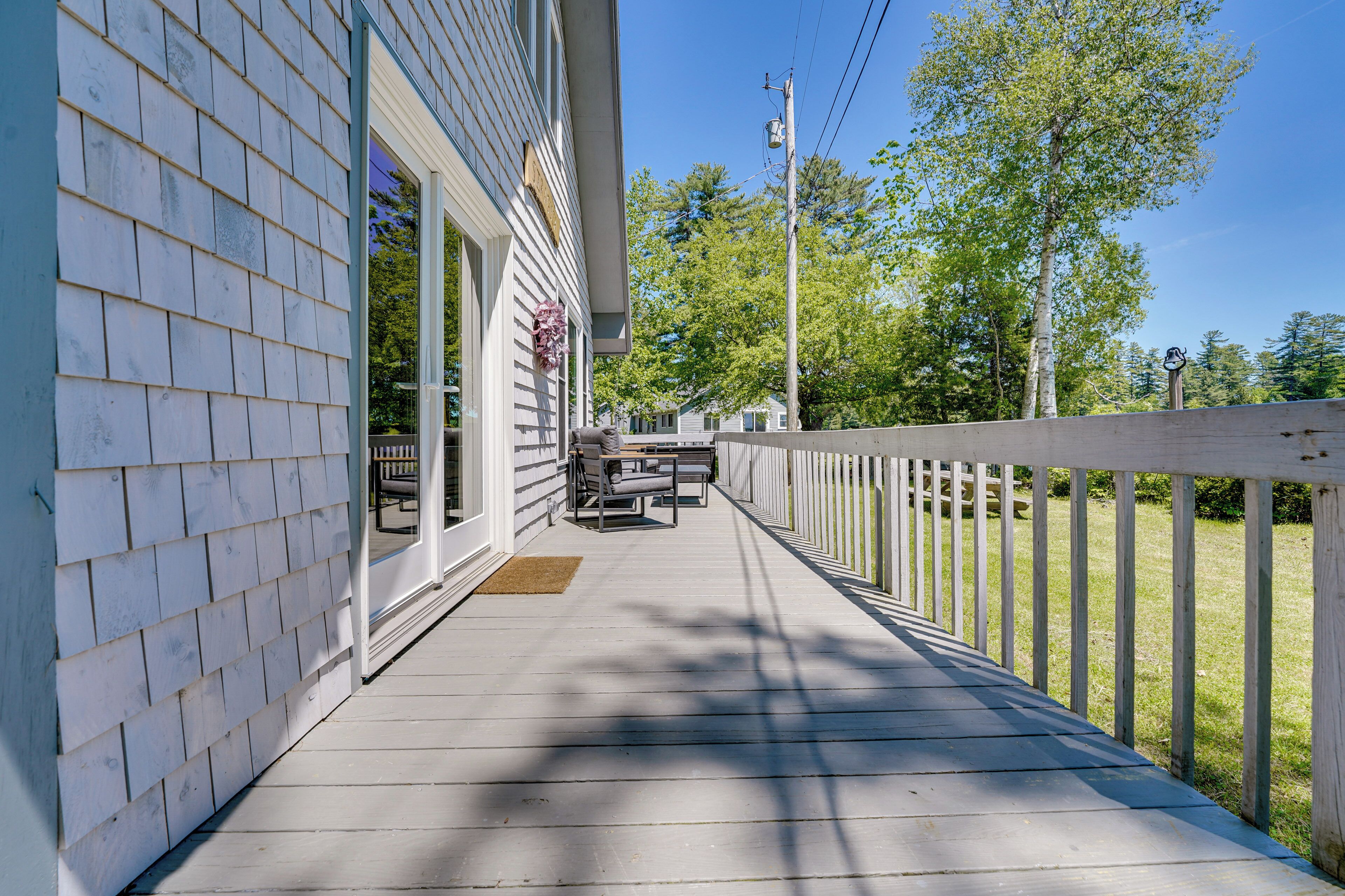 A wooden deck with a railing, a bench, and a door leading to a covered porch.