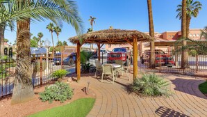 A patio area with a thatched gazebo, outdoor seating, and palm trees. - Walk to Rotary Park: LHC Condo w/ Private Patio (Lake Havasu City)