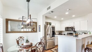 A modern kitchen with white cabinets, stainless steel appliances, and a glass dining table with ornate chairs. - Walk to Rotary Park: LHC Condo w/ Private Patio (Lake Havasu City)
