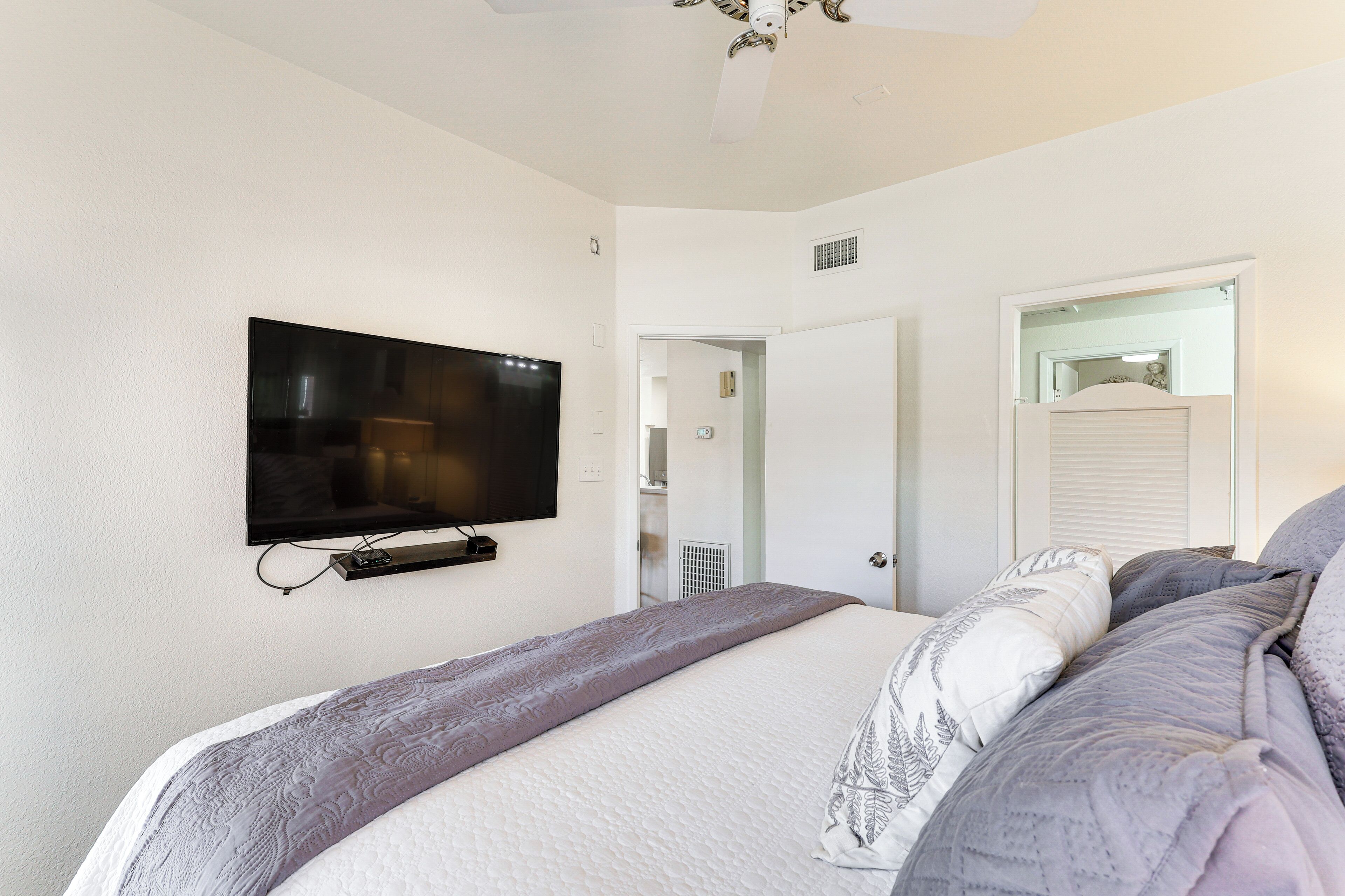 A bedroom with a bed, a television mounted on the wall, and a door leading to another room.