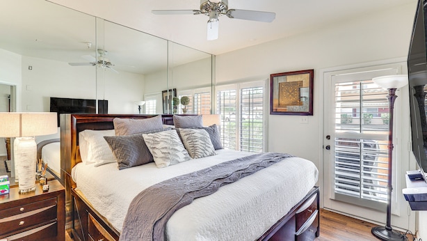 A bedroom with a large bed, a ceiling fan, a TV, and a door with blinds. - Walk to Rotary Park: LHC Condo w/ Private Patio (Lake Havasu City)