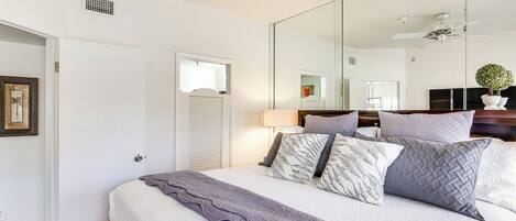 A bedroom with a large bed, a ceiling fan, a mirror, and a door.