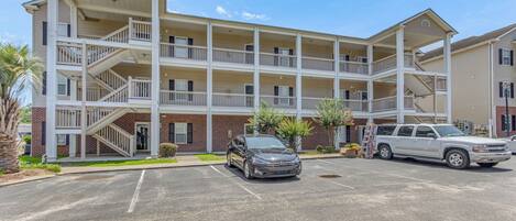 A multi-story motel with a central atrium, multiple balconies, and a parking lot with two vehicles.