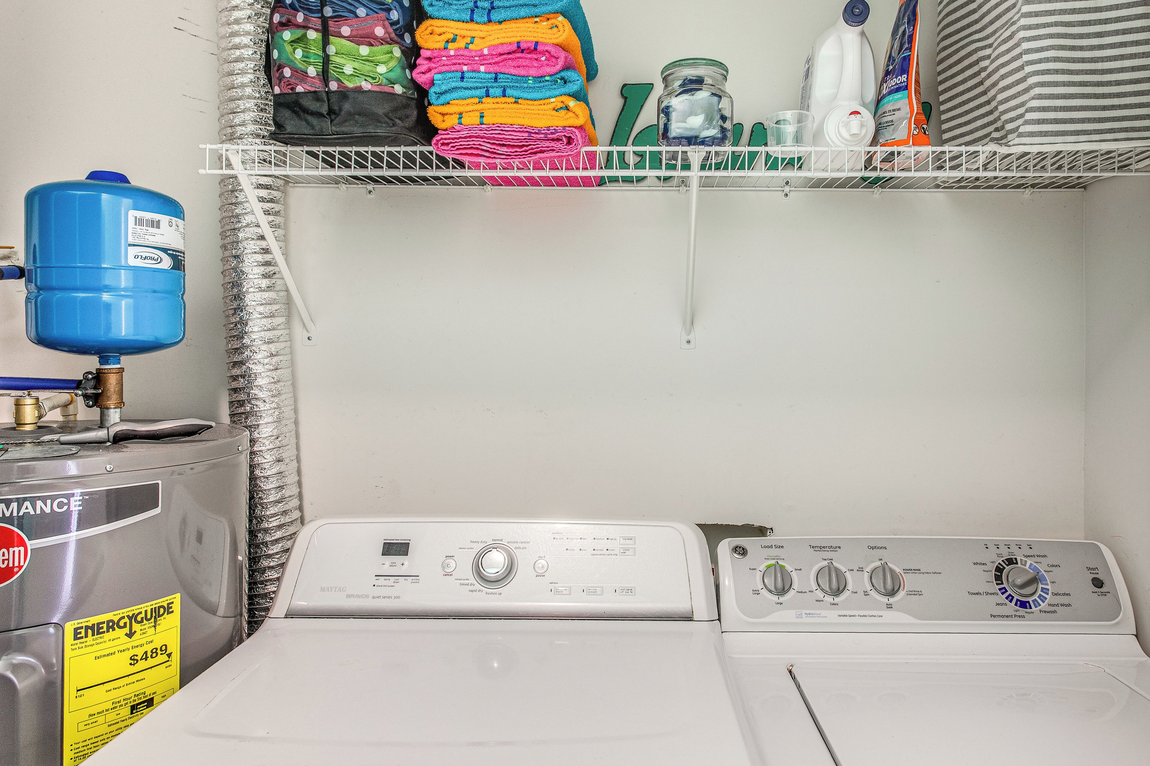 A laundry area with a water heater, stacked towels, and cleaning supplies.
