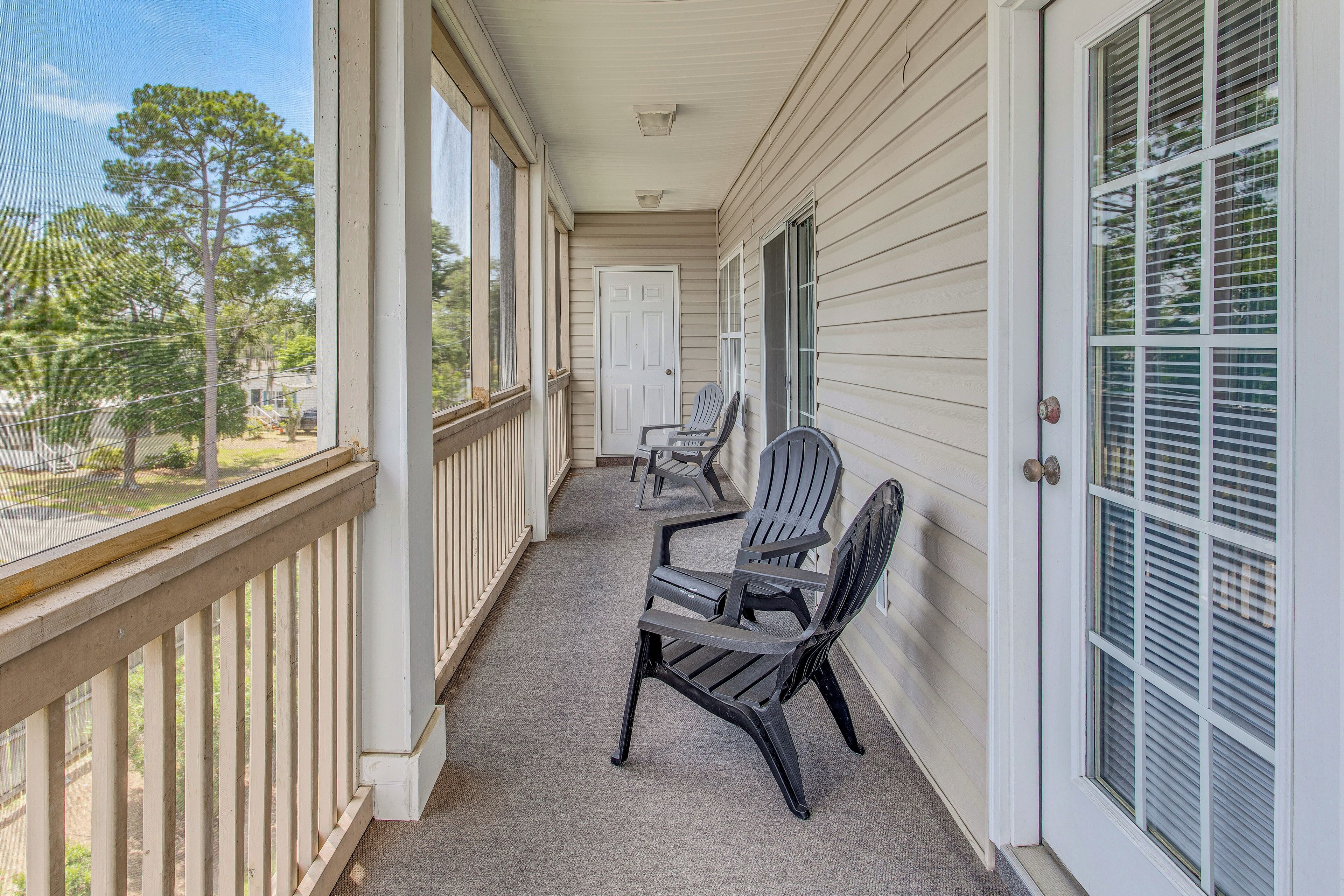 A covered porch with two chairs, a door, and a view of the neighborhood.