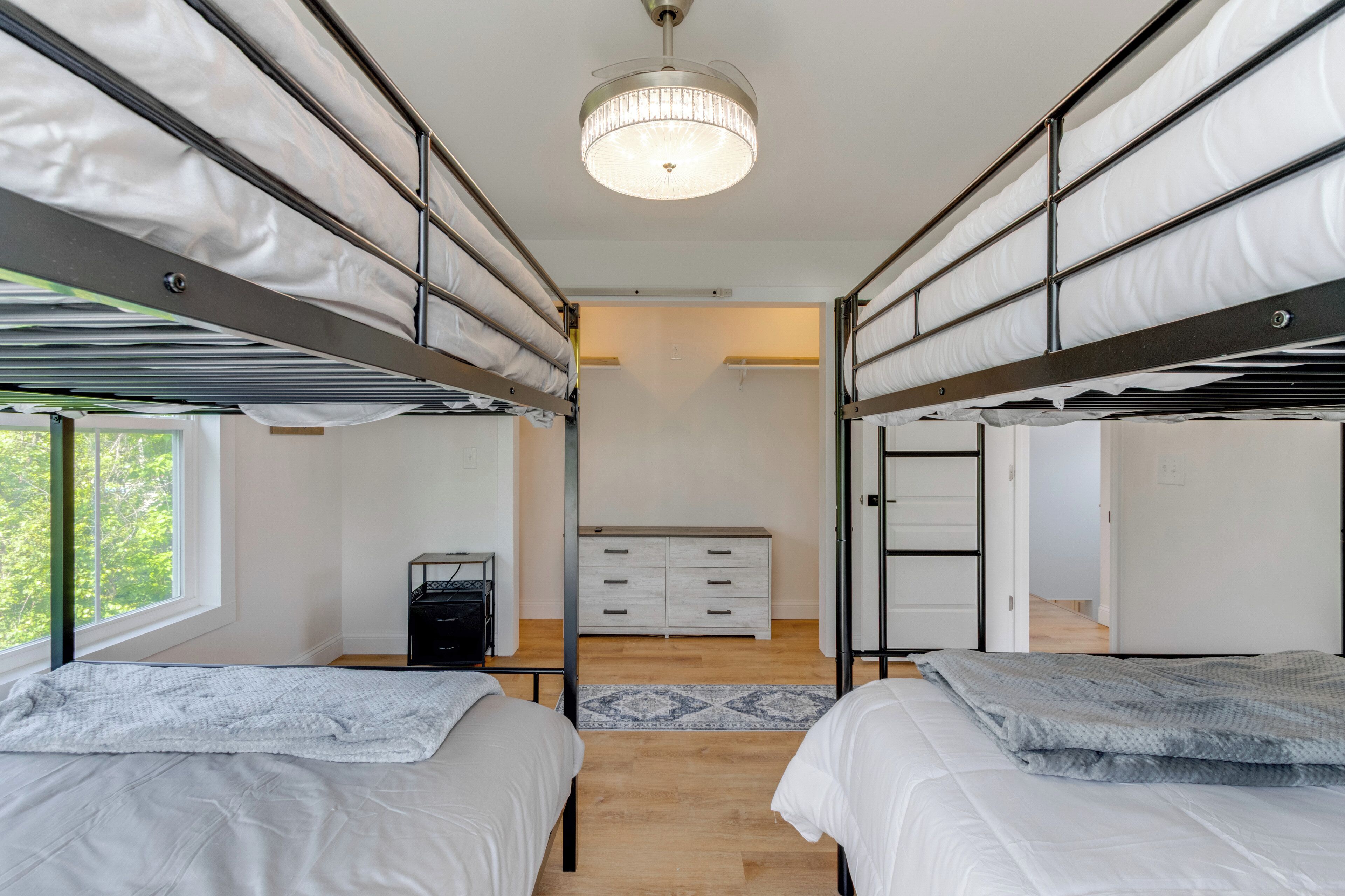 A bunk bed room with a ceiling light, a dresser, and a window.