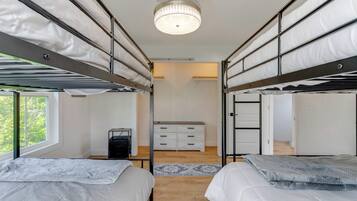 A bunk bed room with a ceiling light, a dresser, and a window.