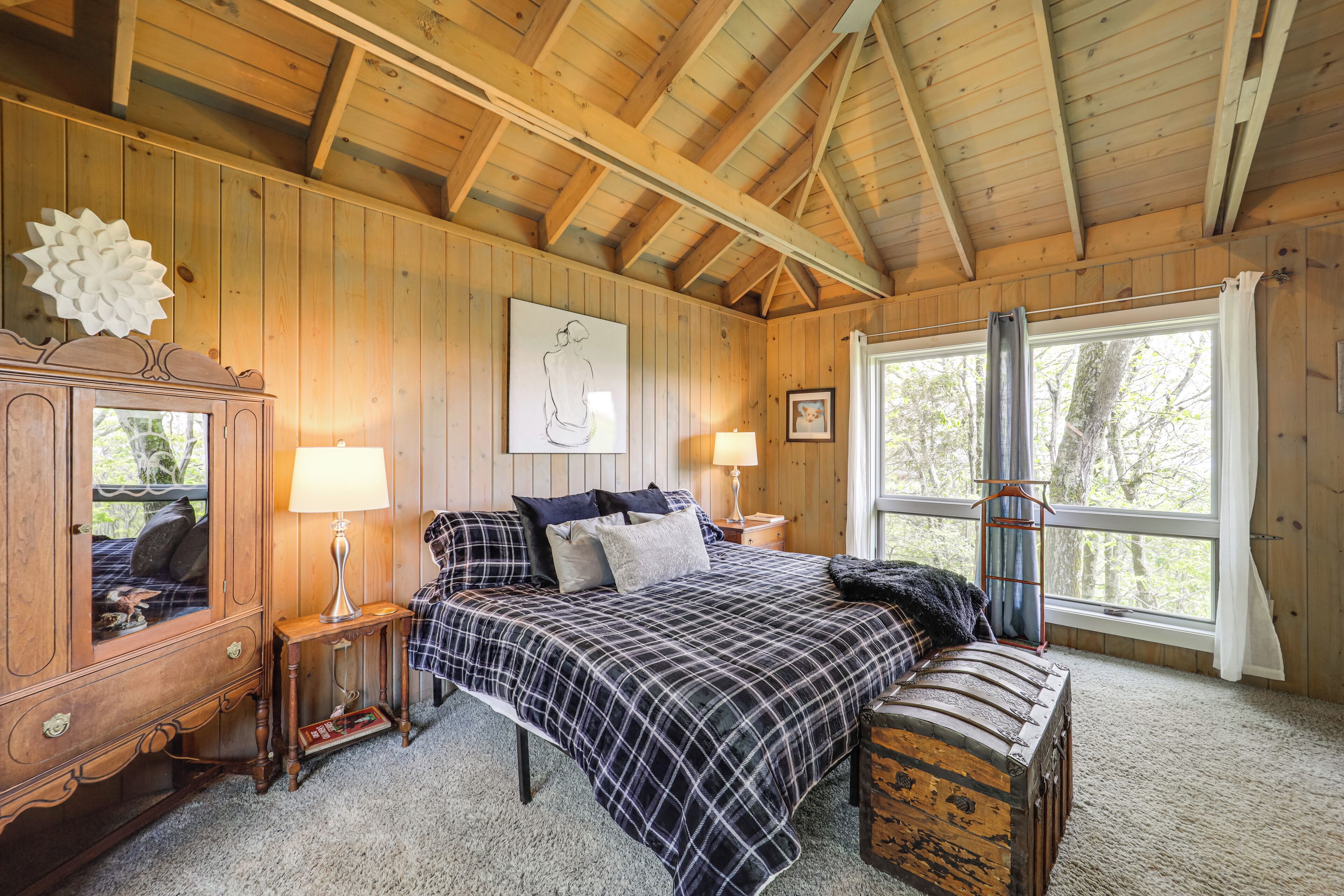 Ein Schlafzimmer in einer Holzhütte mit einem Bett, Nachttischen, einer Kommode und einem großen Fenster.