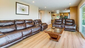 A spacious living room with a brown leather sectional sofa, a glass coffee table, and wooden flooring.