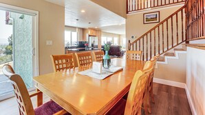 A dining area with a wooden table and chairs, a kitchen in the background, and a staircase with wooden railings.