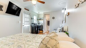 A bedroom with a bed, a ceiling fan, a TV mounted on the wall, and a kitchenette in the background. - Hike, Fish & More: Cozy Studio w/ Yard in Augusta! (Augusta)