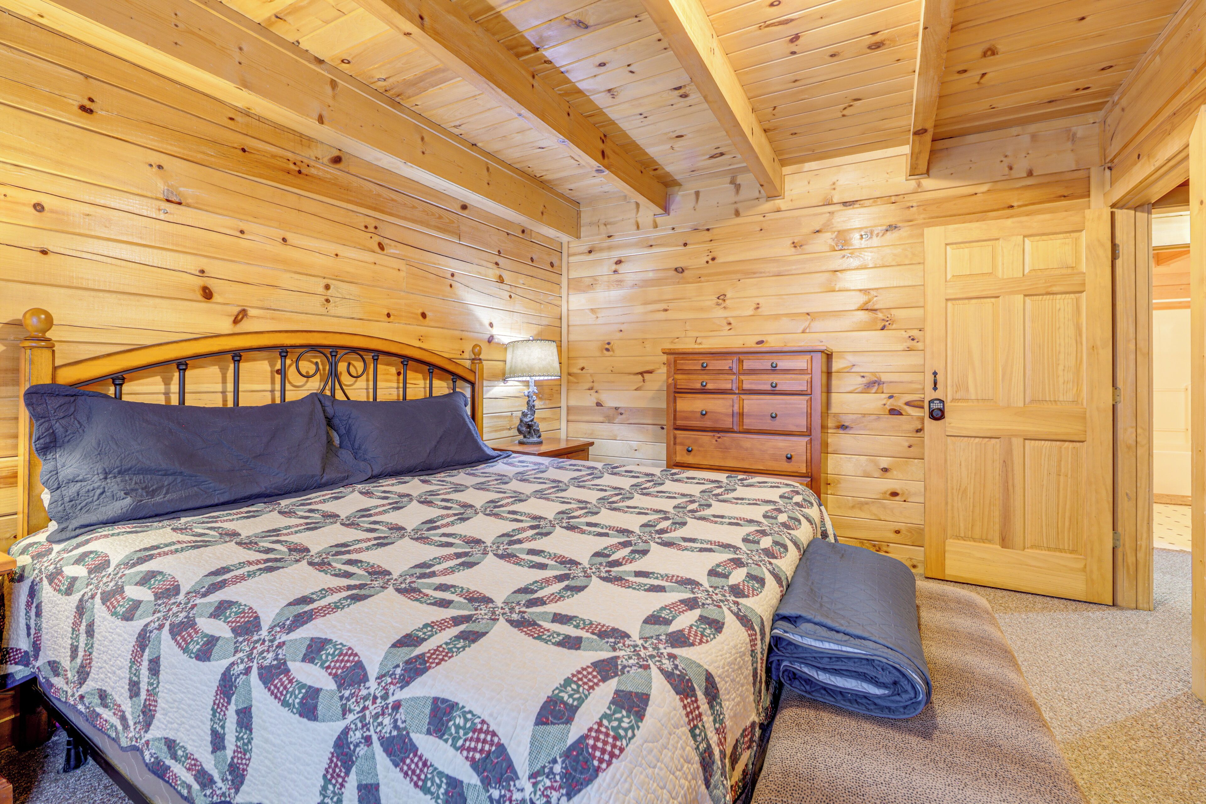 A wooden cabin bedroom with a bed, dresser, and a door.