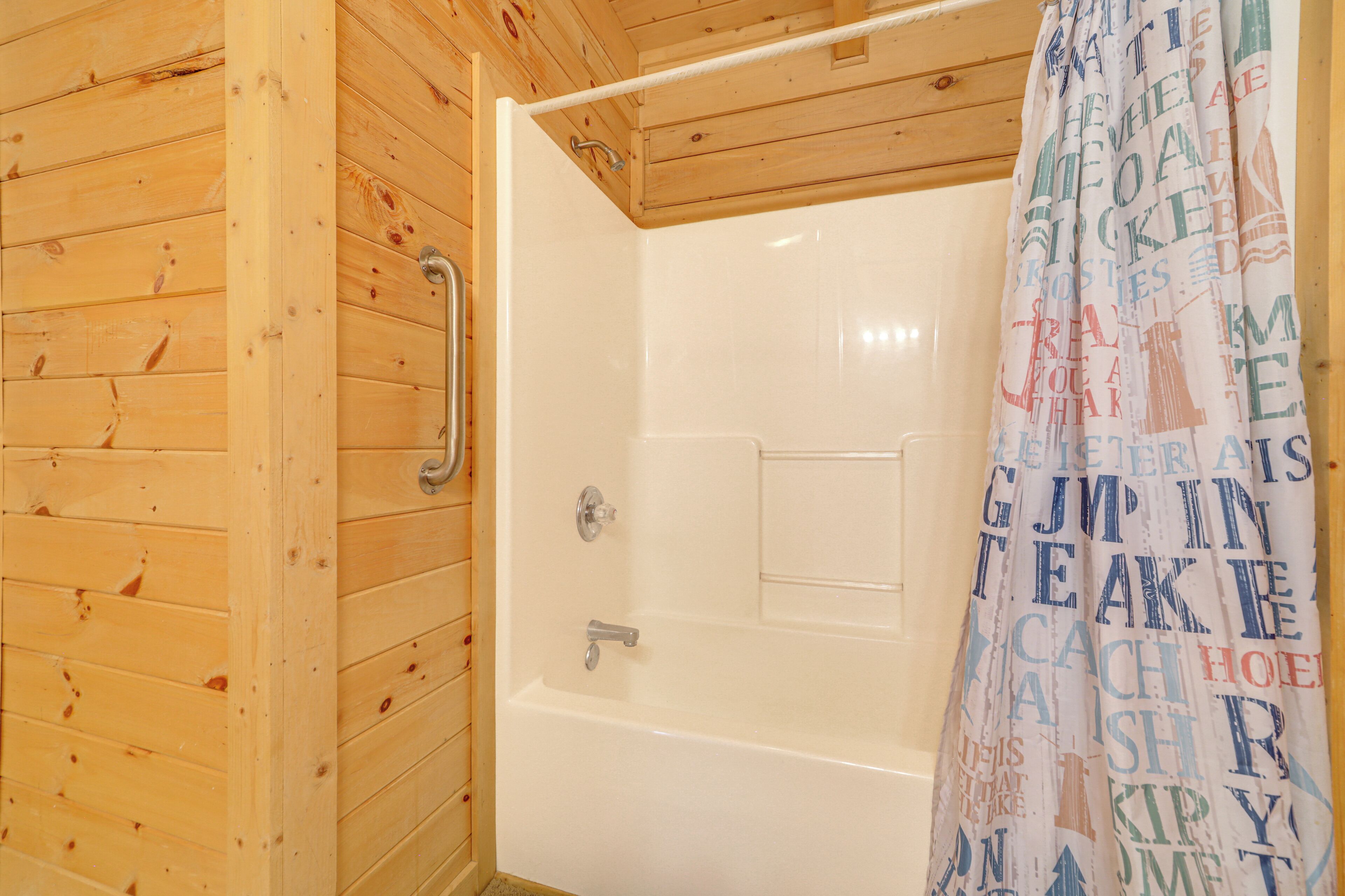 Ein Badezimmer einer Holzhütte mit einer Badewanne, einer Duschvorhang mit Aufschrift und einer Holztür.