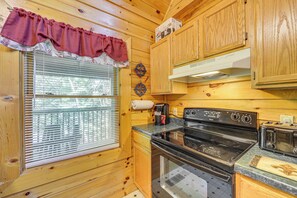 A compact kitchen with wooden cabinets, a stove, a toaster, and a window with blinds. - Smokies Cabin on Douglas Lake w/ Resort Pool (Sevierville)