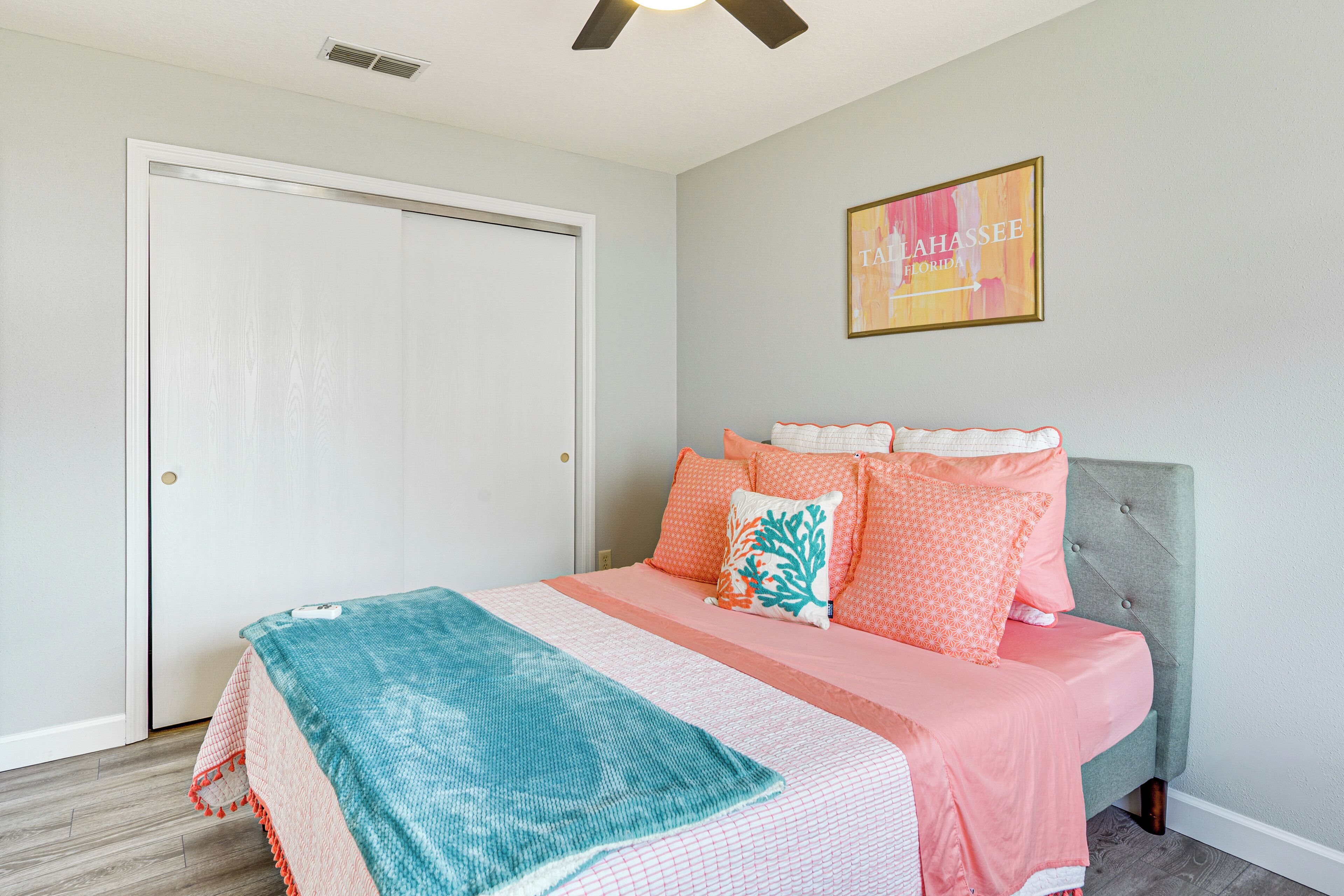 A bedroom with a bed, a ceiling fan, a door, and a wall with a framed picture.