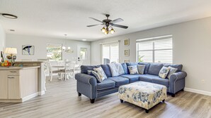 A spacious living room with a sectional sofa, ottoman, and a dining area with a white table and chairs. - 6 Mi to Lake Sumter Landing: Home w/ Perks! (The Villages)