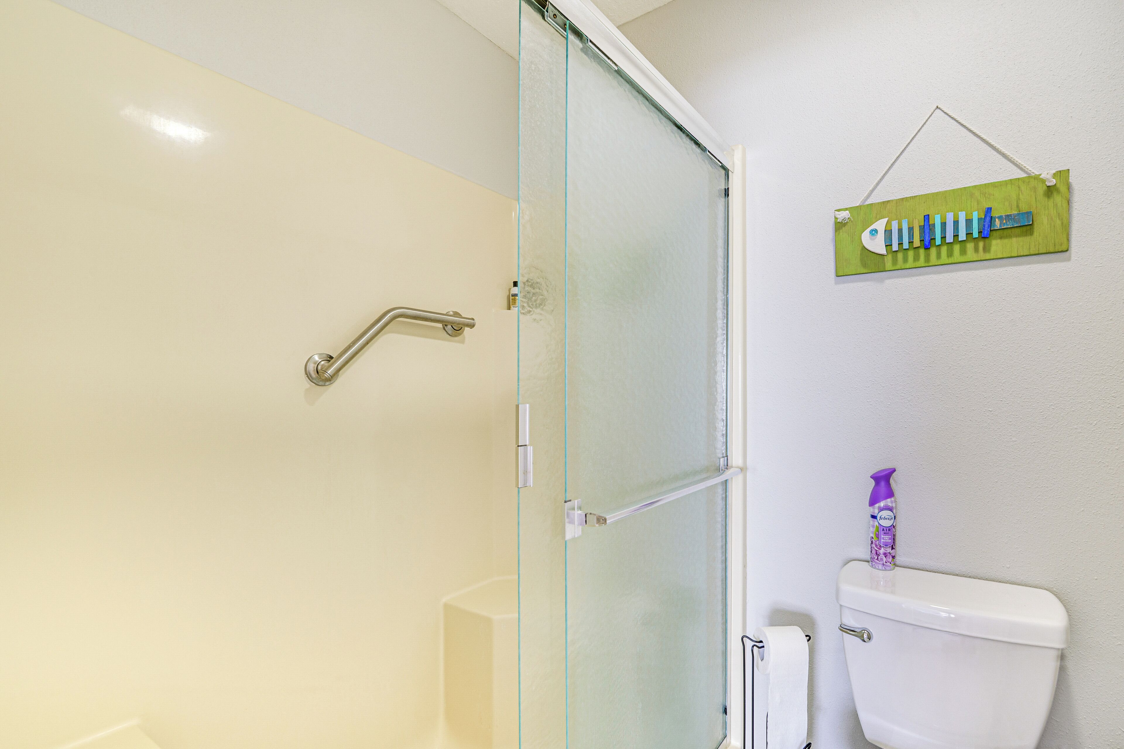Een badkamer met een douchecabine van glas, een toilet en een tandenborstelhanger aan de muur.