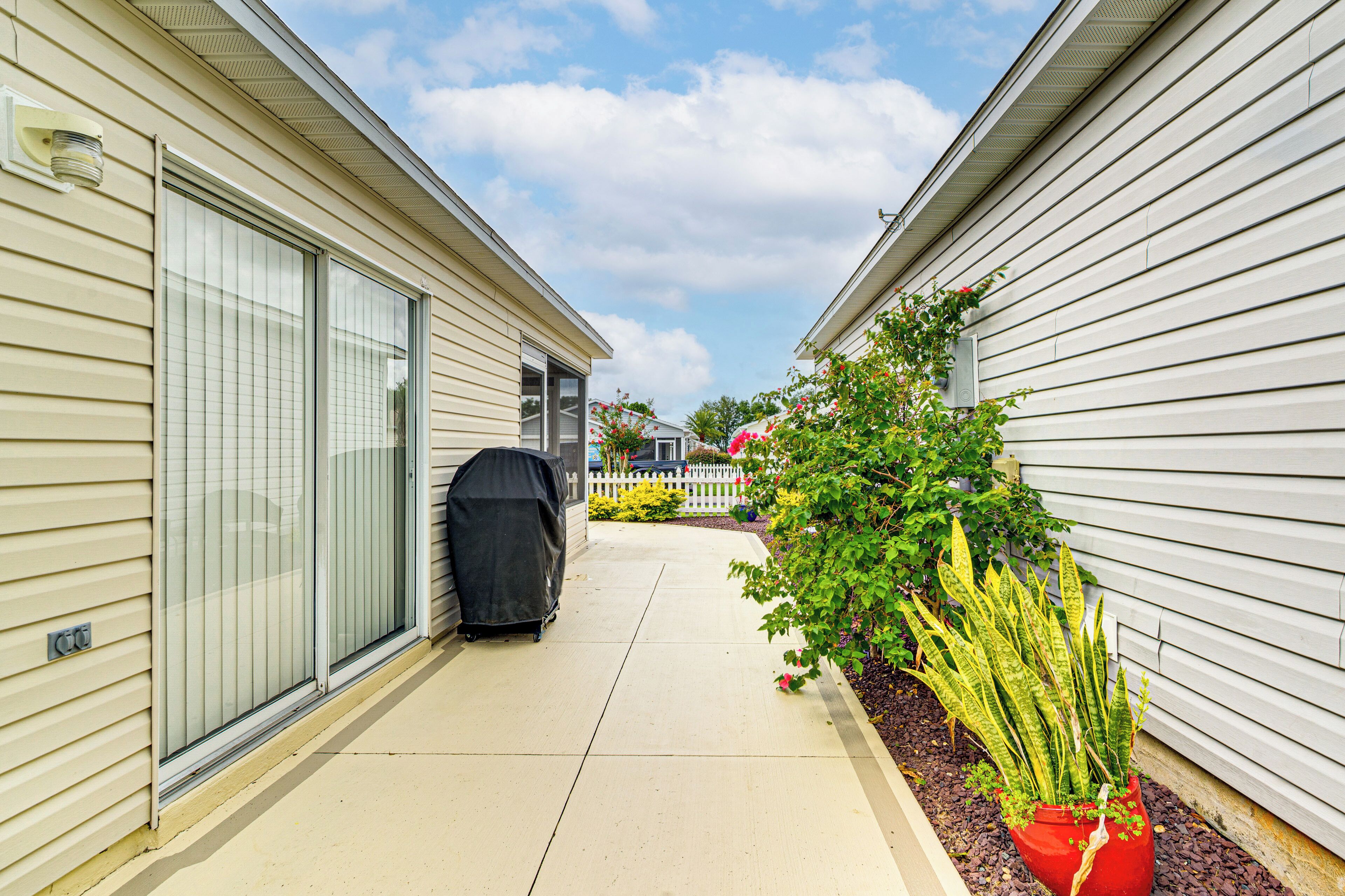 A narrow pathway between two buildings with a barbecue grill and a potted plant.