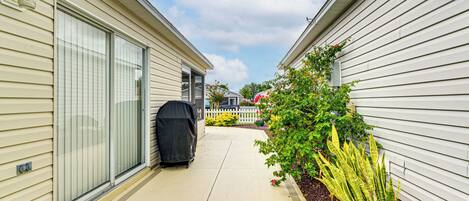 A narrow pathway between two buildings with a barbecue grill and a potted plant.