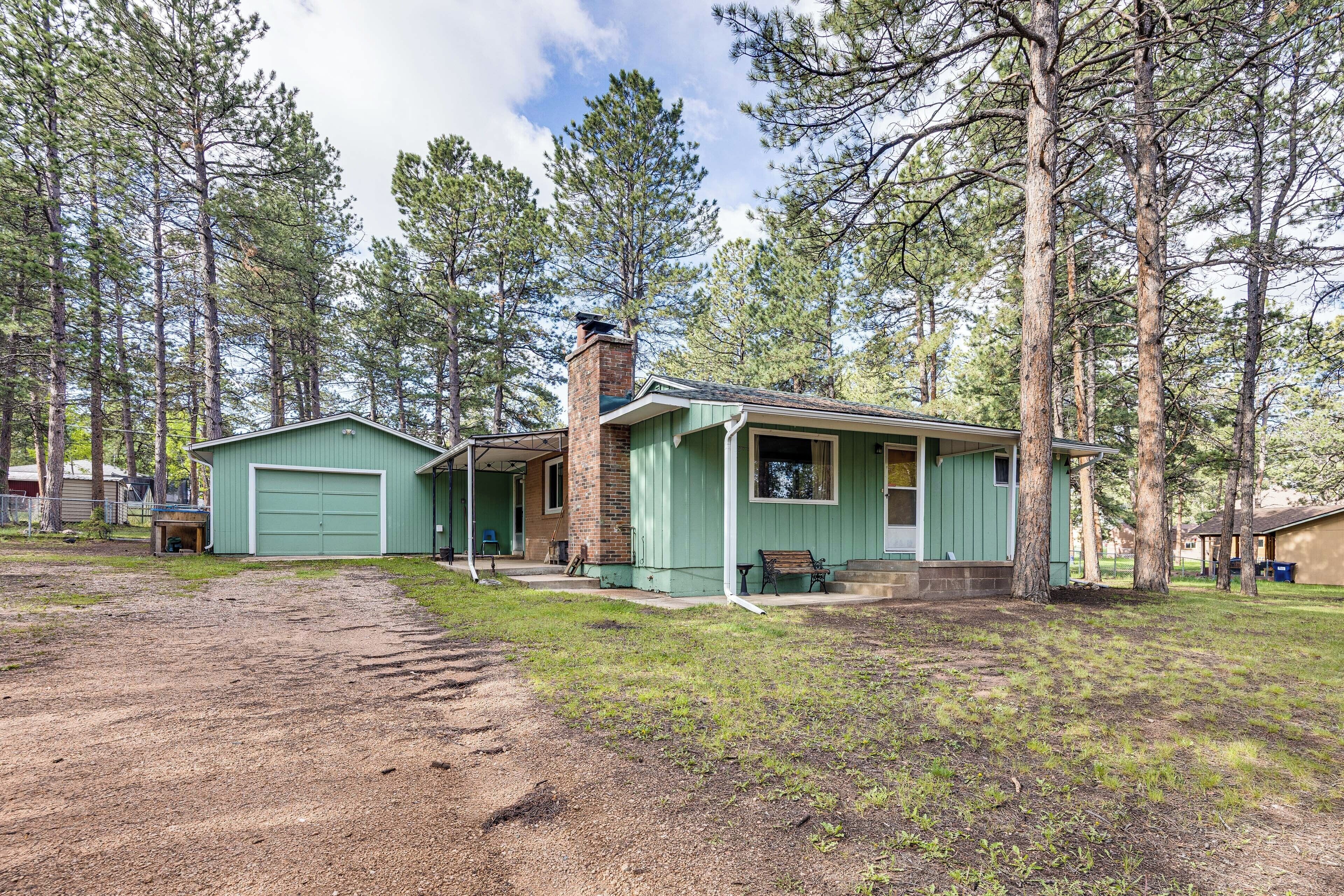 A single-story house with a green garage, a brick chimney, and a porch with a bench.