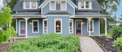 A two-story house with a front porch, a pathway leading to the entrance, and a well-maintained garden.