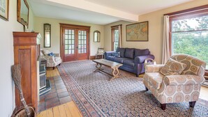 A spacious living room with a patterned rug, a blue sofa, a patterned armchair, and a wooden coffee table. - 2 Mi to Chardon Square: Family Farmhouse Escape (Chardon)