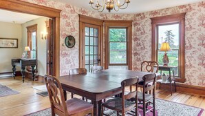 A dining room with a wooden table and chairs, a chandelier, and floral wallpaper. - 2 Mi to Chardon Square: Family Farmhouse Escape (Chardon)
