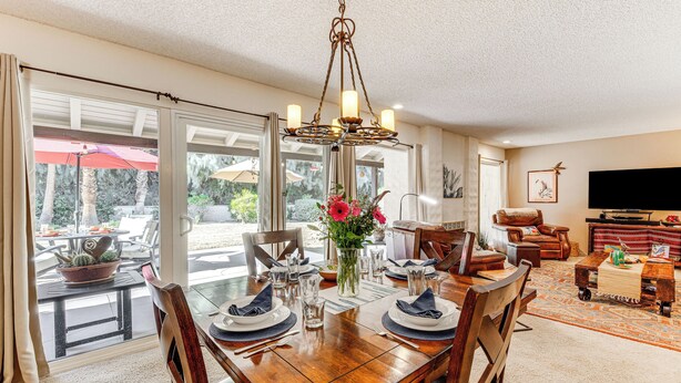 A dining area with a wooden table set for four, a chandelier, and a view of the outdoors.