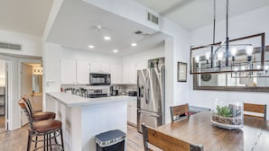 A modern kitchen with white cabinets, stainless steel appliances, and a wooden dining table with chairs. - 1 Mi to Beach: Lake Havasu City Condo w/ Balcony (Lake Havasu City)