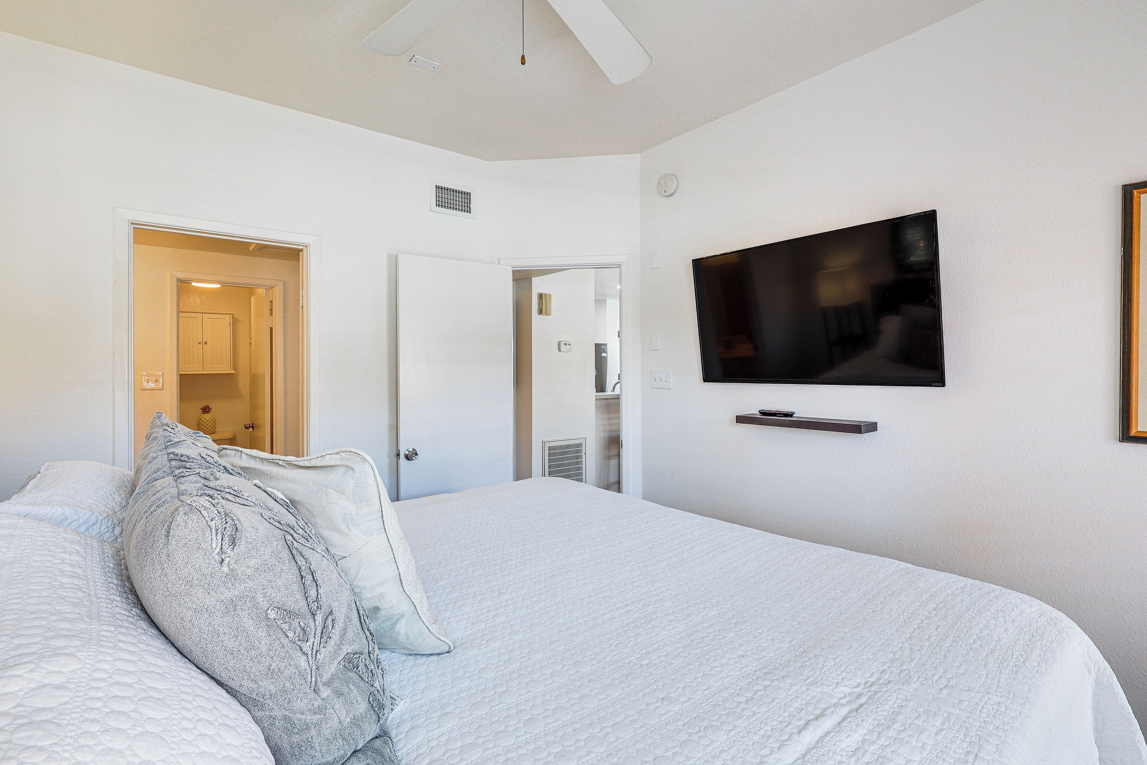 A bedroom with a large bed, a flat-screen TV mounted on the wall, and a door leading to a bathroom.