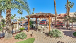 A covered outdoor seating area with a thatched roof, surrounded by palm trees and a brick pathway. - 1 Mi to Beach: Lake Havasu City Condo w/ Balcony (Lake Havasu City)
