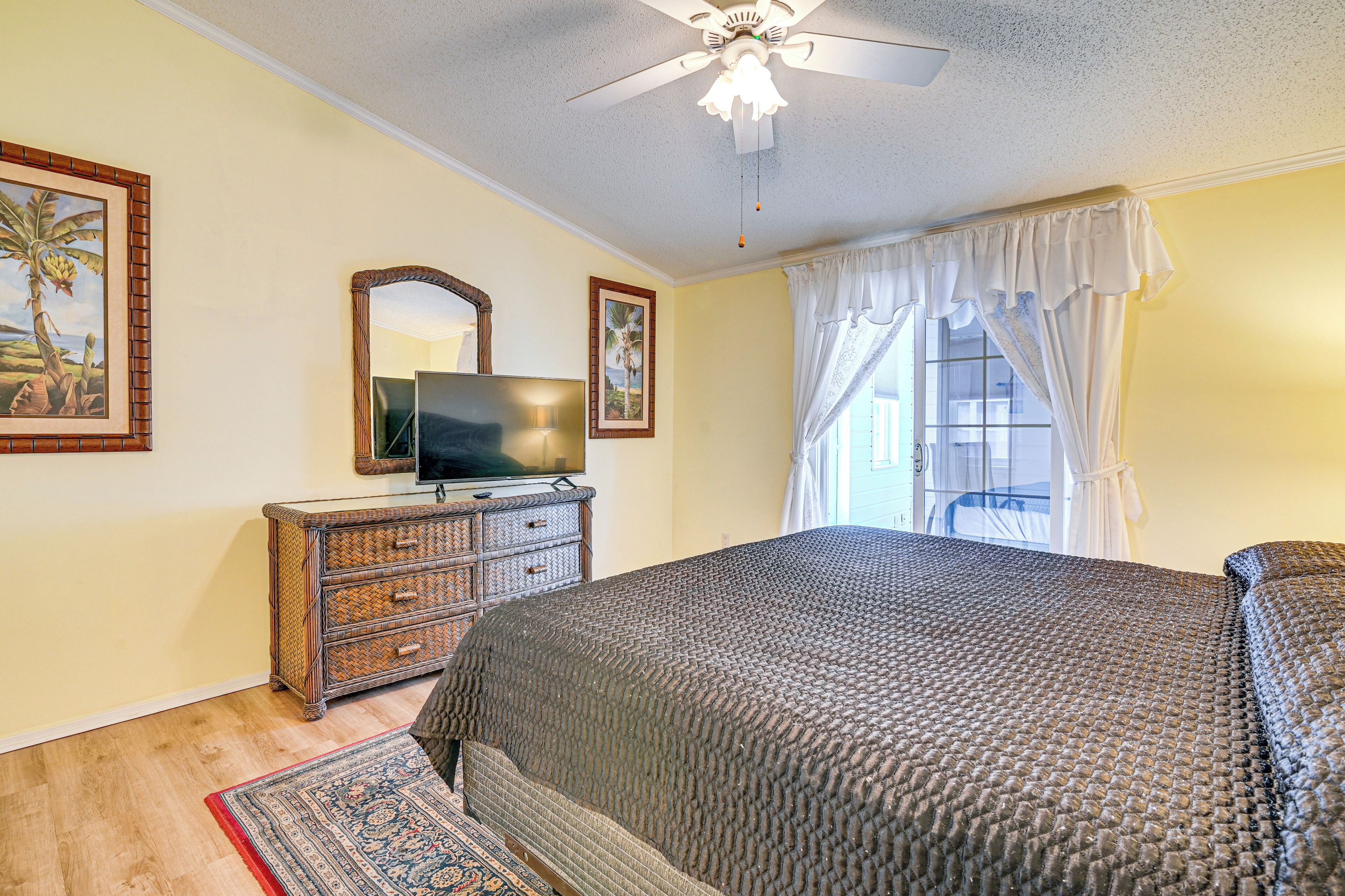A bedroom with a bed, a dresser, a television, and a ceiling fan.
