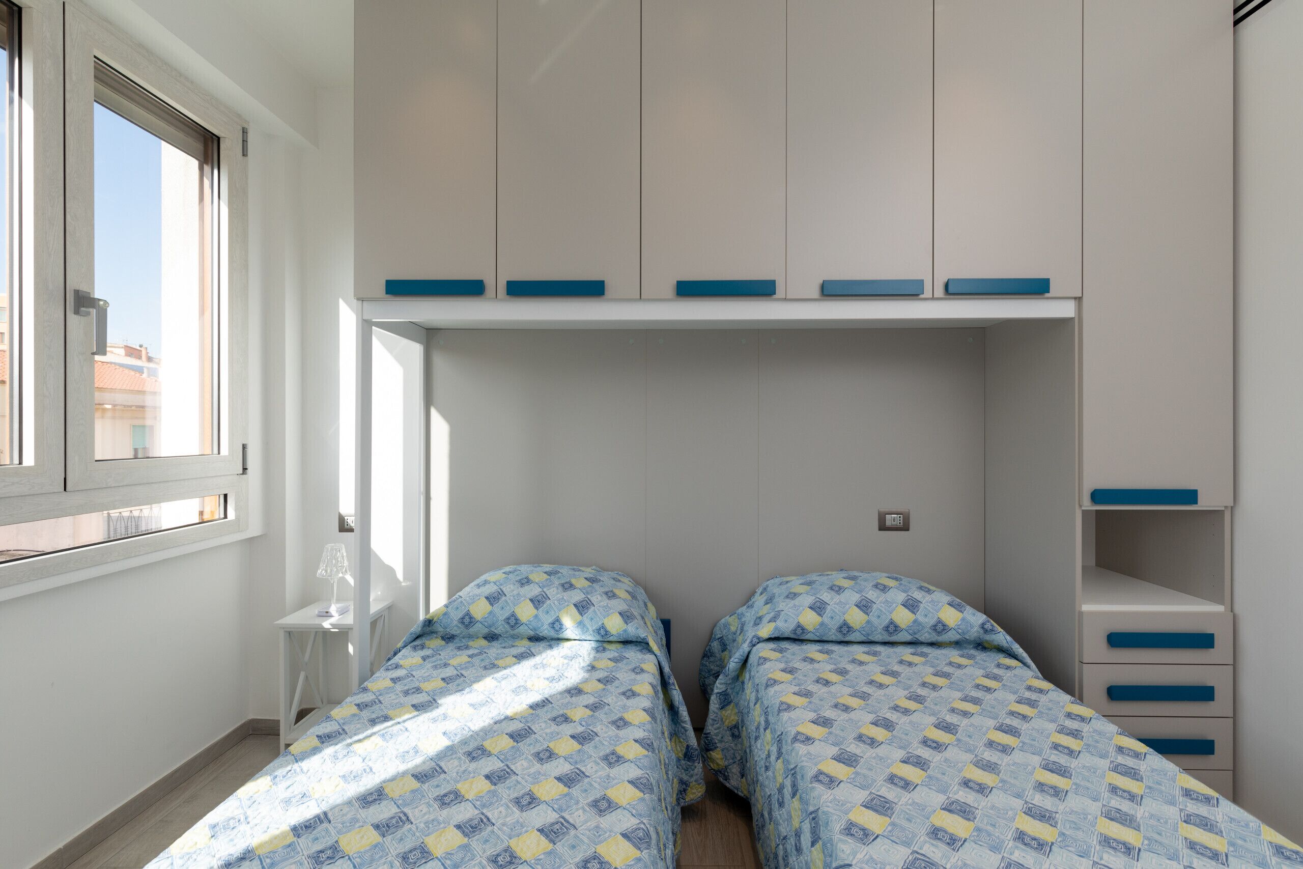 A bedroom with two beds, a window, and built-in storage.