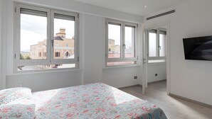 A bedroom with a bed, large windows, and a TV on the wall. - Casa Brezza Marina by Wonderful Italy (Olbia)