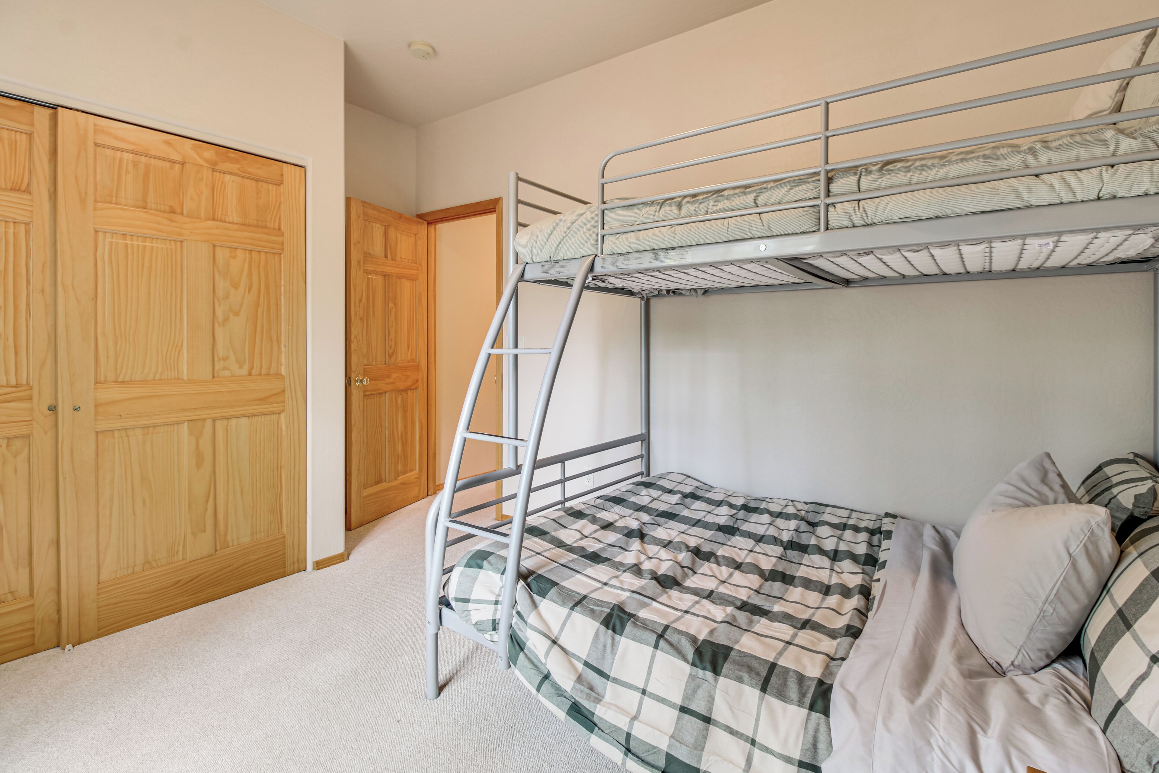 A room with a bunk bed, wooden wardrobe, and carpeted floor.