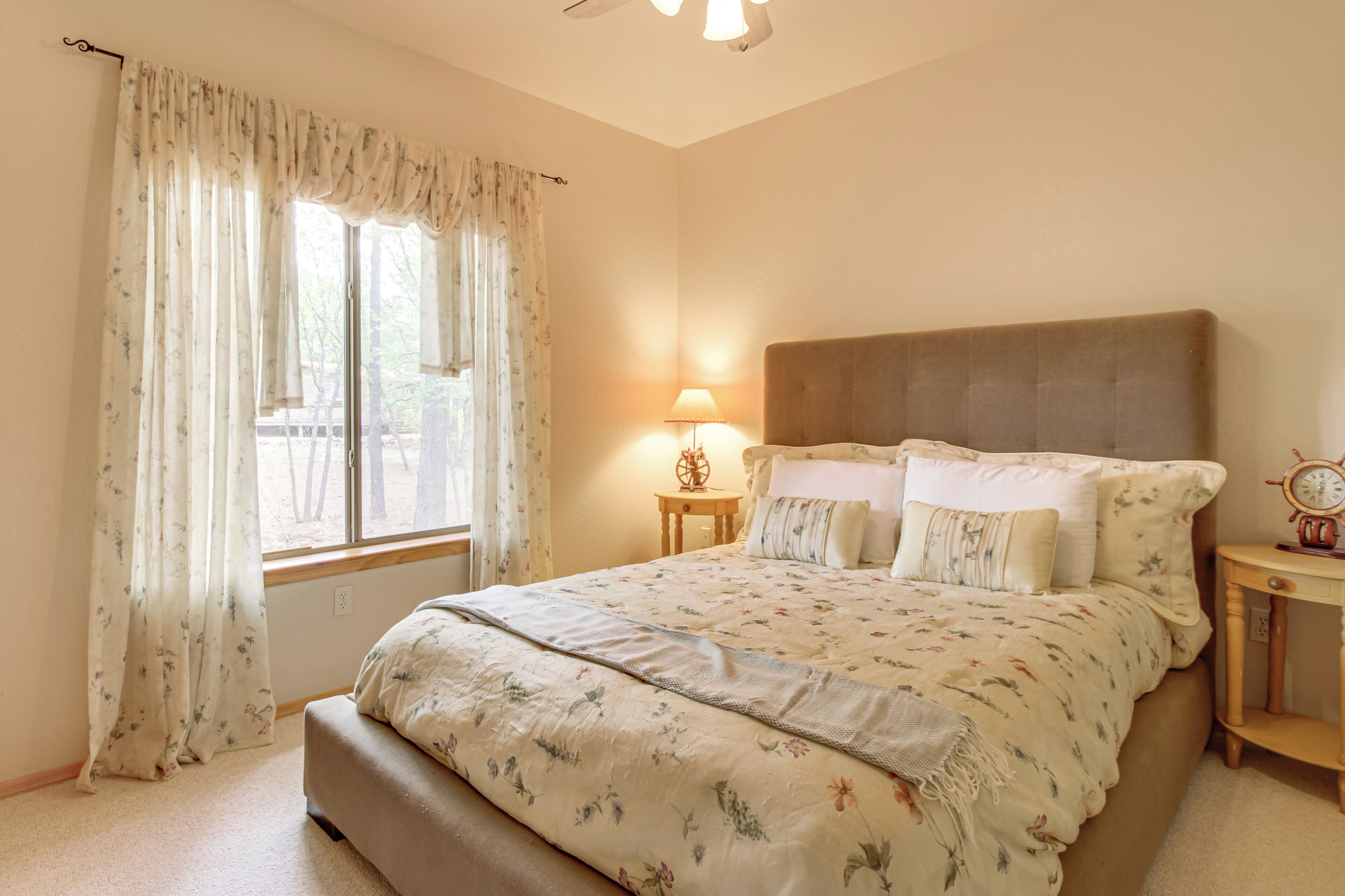 A bedroom with a large bed, a bedside table with a lamp, and a window with curtains.
