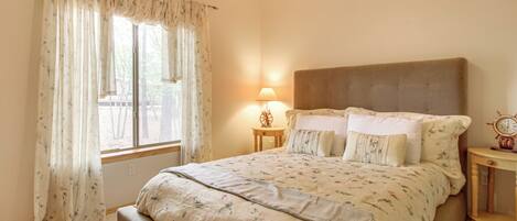 A bedroom with a large bed, a bedside table with a lamp, and a window with curtains.