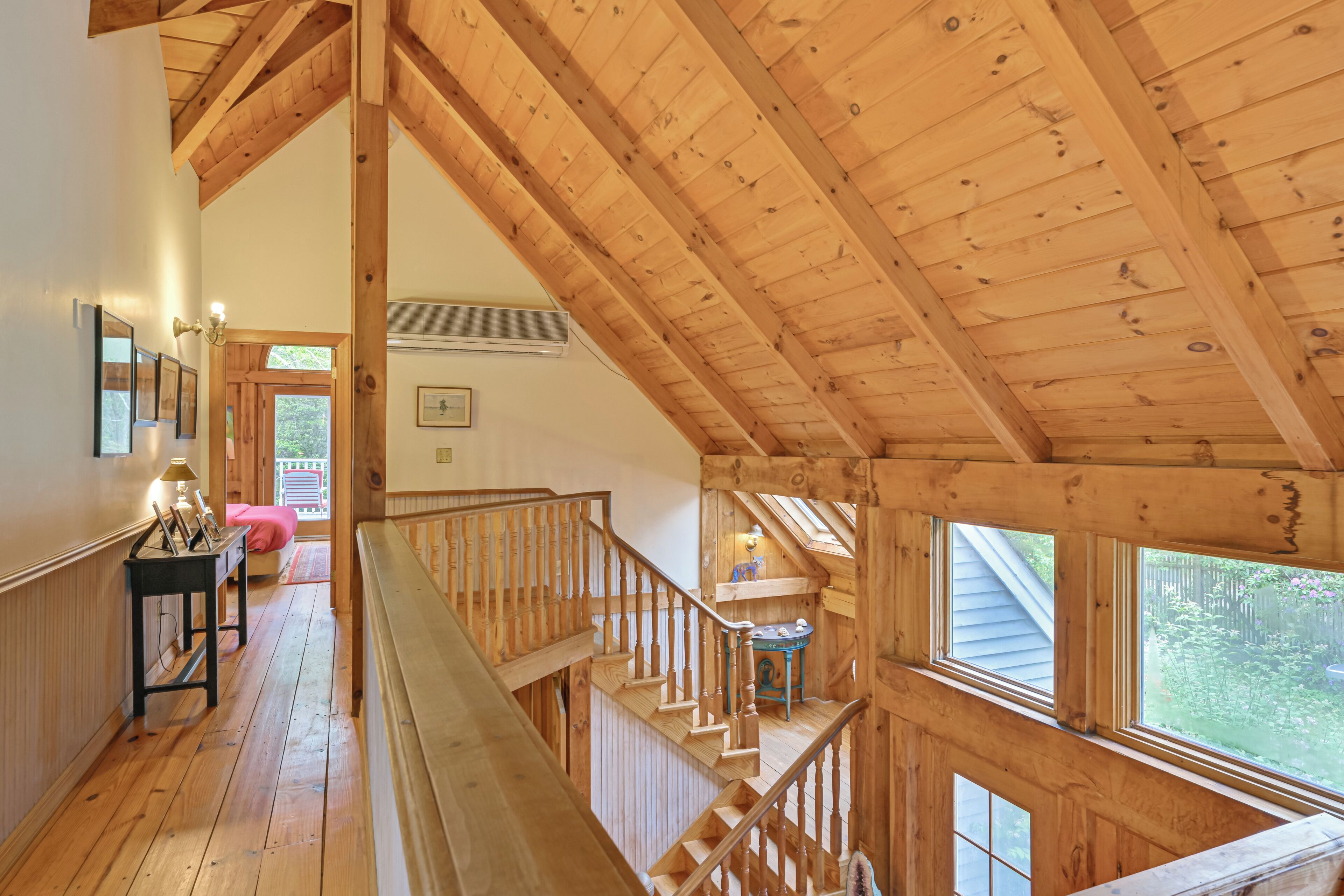 Un escalier en bois mène à une mezzanine offrant une vue sur l’extérieur.