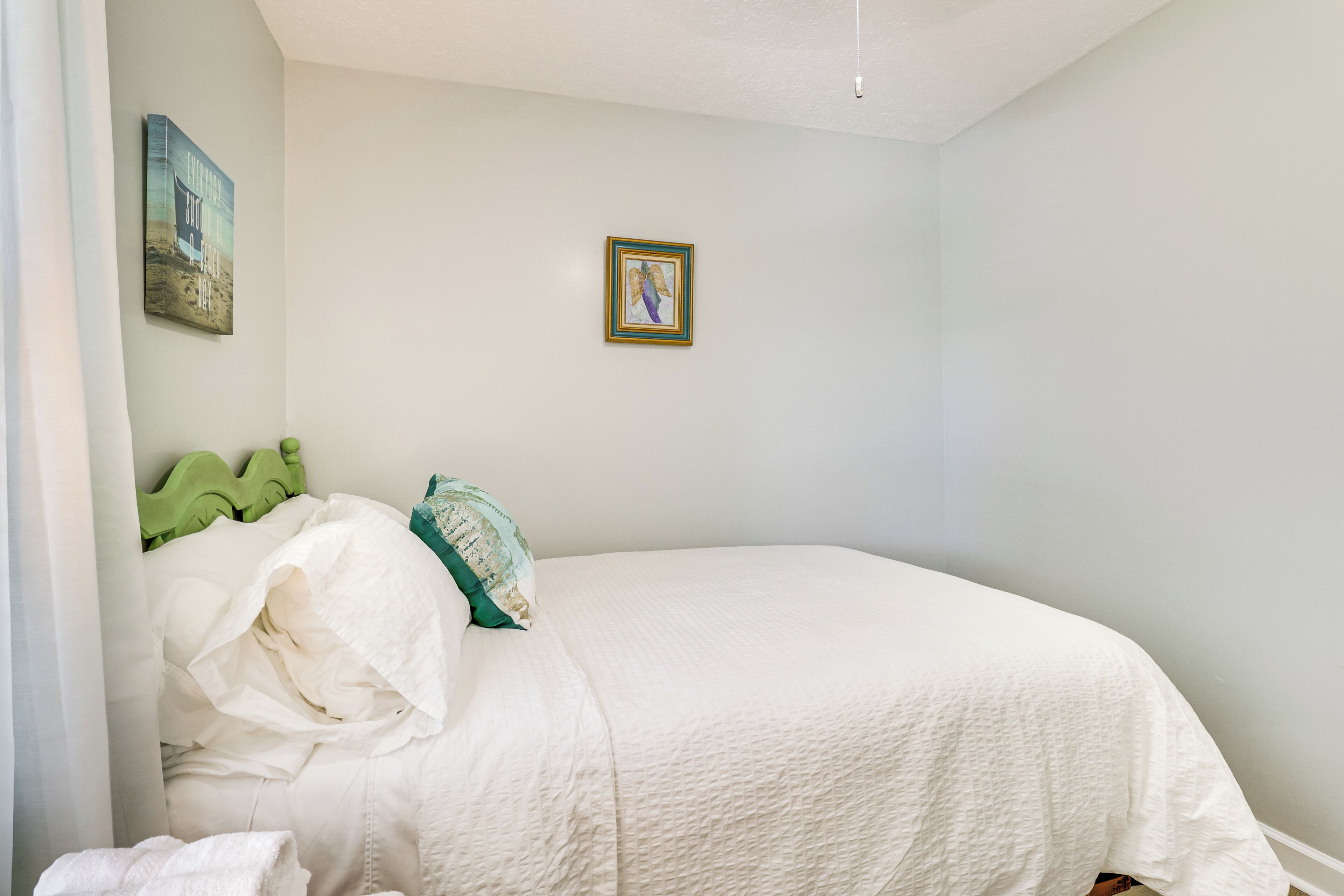 A bedroom with a single bed, a green headboard, a framed picture on the wall, and a white curtain.