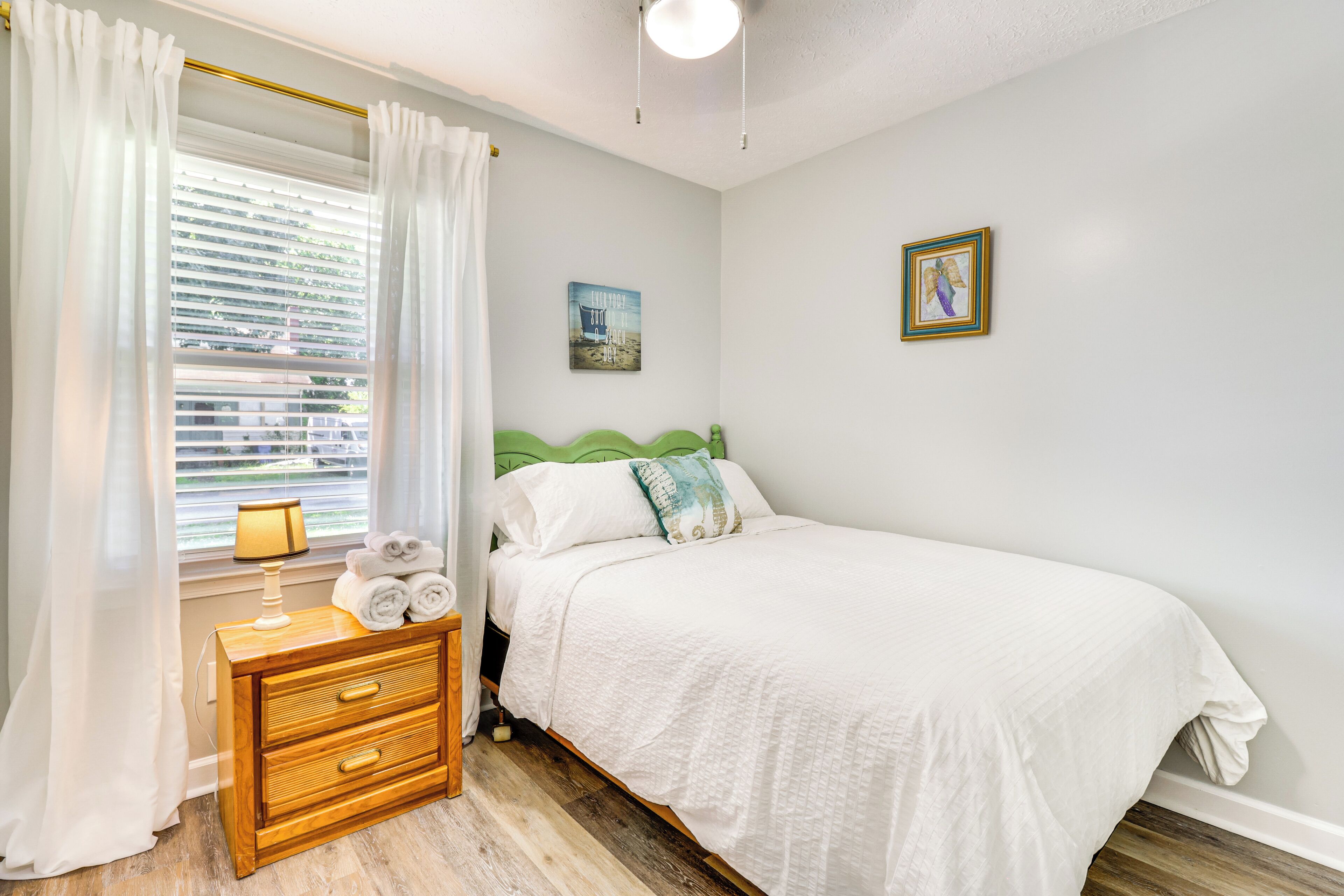A bedroom with a bed, a nightstand, a lamp, and a window with curtains.