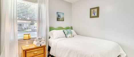 A bedroom with a bed, a nightstand, a lamp, and a window with curtains.