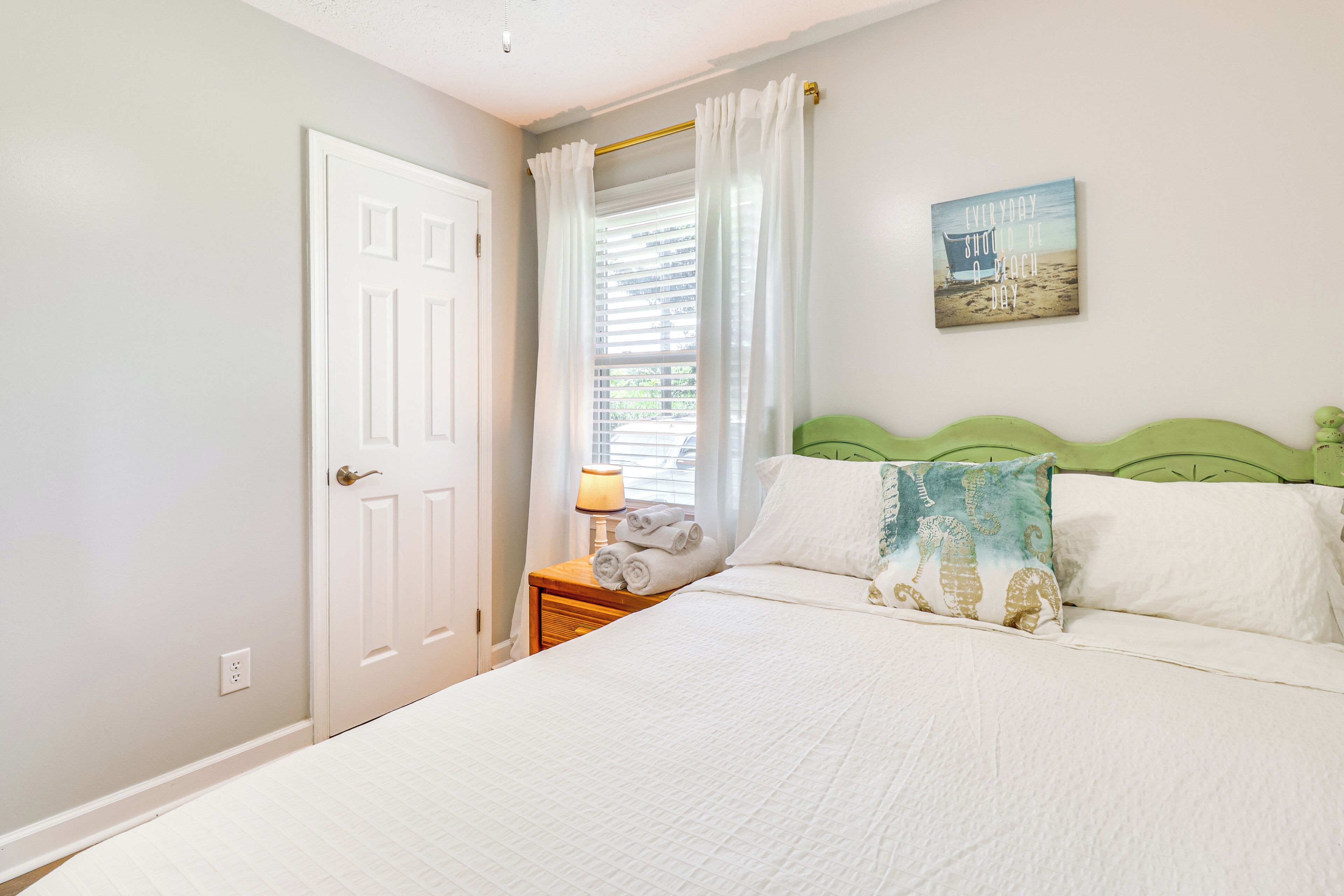 A bedroom with a bed, a nightstand, a lamp, a door, and a window with curtains.
