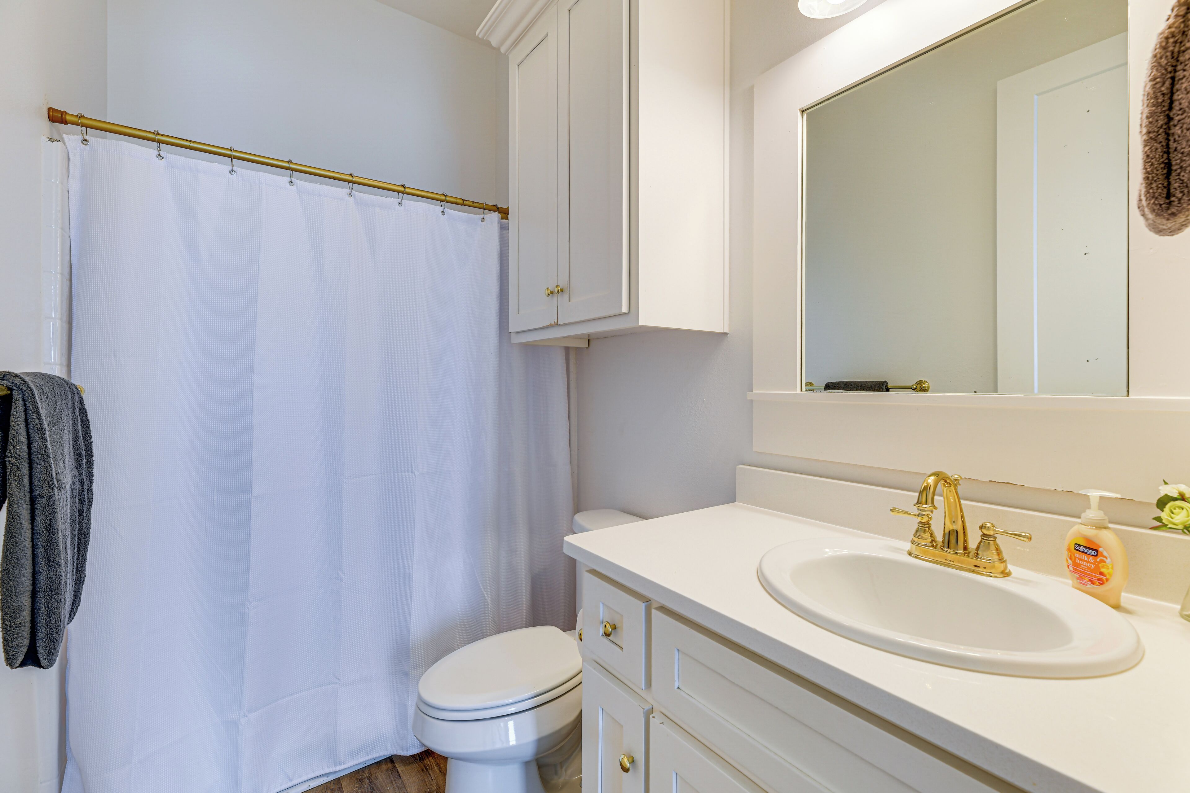 A bathroom with a white toilet, a white sink with a gold faucet, and a white shower curtain.